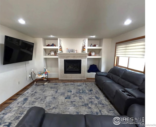 living area with built in shelves, a tiled fireplace, and wood finished floors