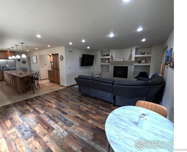 living room with built in shelves, light wood-style flooring, recessed lighting, a fireplace, and visible vents