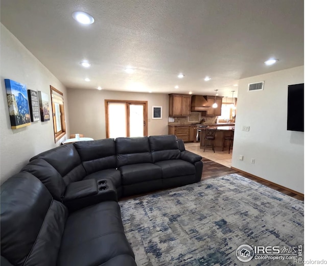 living room with baseboards, a textured ceiling, visible vents, and recessed lighting