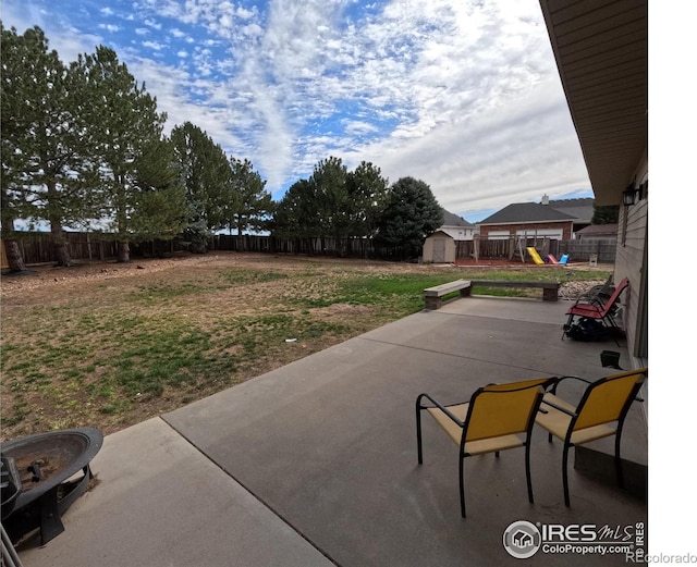 view of patio / terrace with a storage shed, a playground, a fenced backyard, and an outbuilding