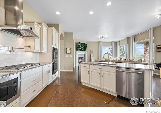 kitchen with light stone counters, sink, wall chimney exhaust hood, dark wood-type flooring, and appliances with stainless steel finishes