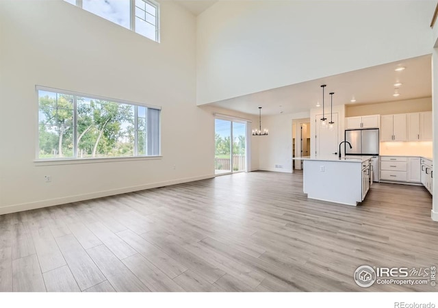 unfurnished living room featuring a healthy amount of sunlight, a towering ceiling, and light hardwood / wood-style flooring