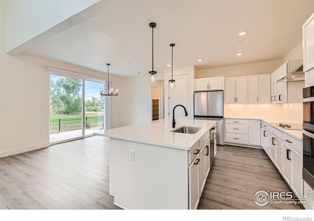 kitchen with white cabinets, sink, light stone countertops, and an island with sink