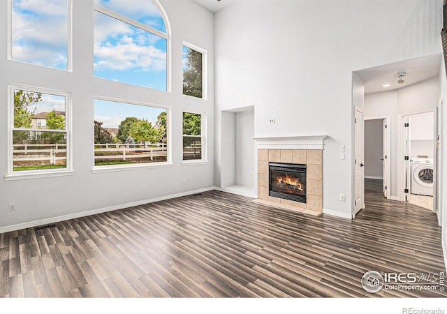 unfurnished living room with a tile fireplace, dark hardwood / wood-style flooring, a towering ceiling, and washer / dryer