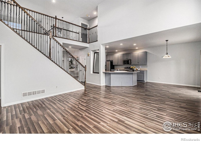 unfurnished living room with dark wood-type flooring and a towering ceiling