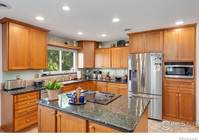 kitchen with appliances with stainless steel finishes, dark stone counters, a center island, and sink