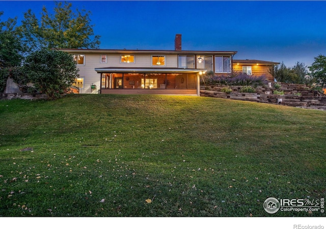 rear view of property featuring a sunroom, a lawn, and a chimney