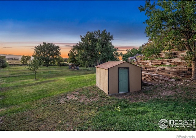 outdoor structure at dusk featuring a storage shed, a lawn, and an outdoor structure