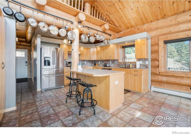 kitchen featuring a baseboard heating unit, stainless steel fridge, decorative backsplash, light brown cabinetry, and a kitchen island