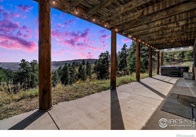 patio terrace at dusk featuring a mountain view and a hot tub