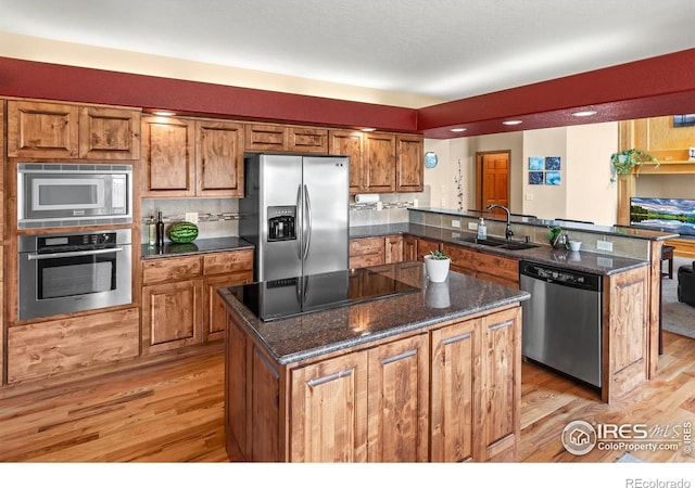 kitchen featuring sink, light hardwood / wood-style flooring, stainless steel appliances, kitchen peninsula, and dark stone counters