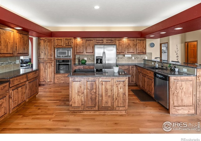 kitchen with sink, light hardwood / wood-style flooring, appliances with stainless steel finishes, kitchen peninsula, and dark stone counters