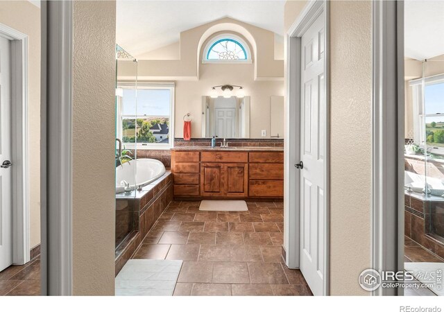 bathroom featuring vaulted ceiling, tiled bath, and vanity