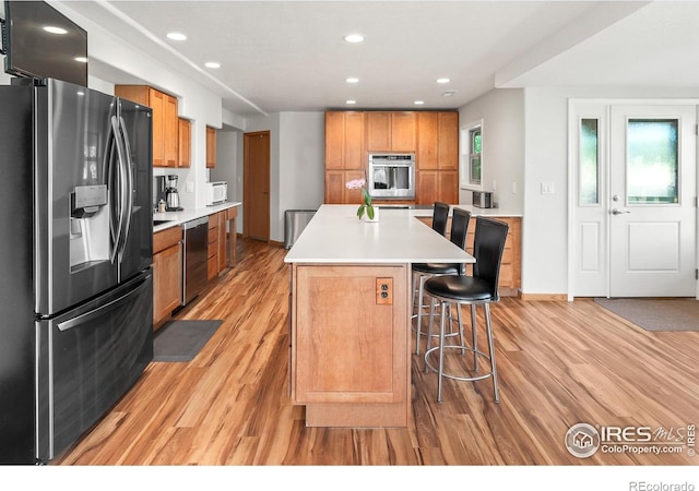 kitchen featuring appliances with stainless steel finishes, a kitchen bar, a center island, and light wood-type flooring