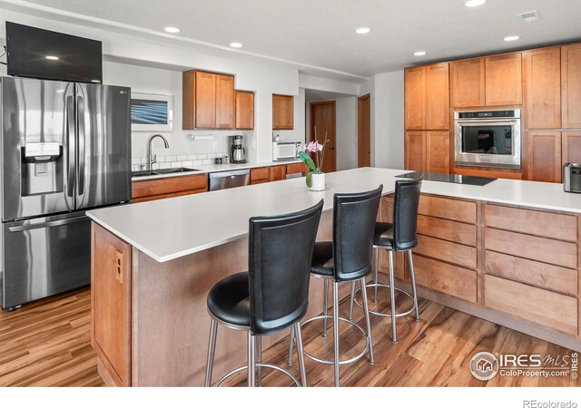 kitchen featuring appliances with stainless steel finishes, a breakfast bar, sink, a center island, and light wood-type flooring