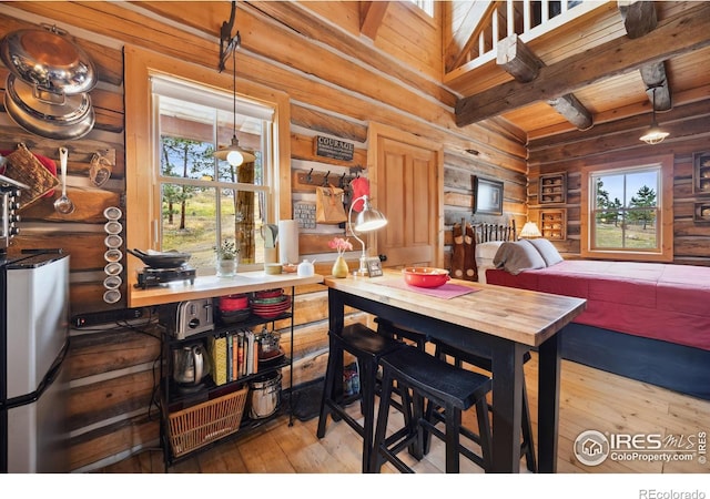 dining room featuring rustic walls, a wealth of natural light, beamed ceiling, and wood-type flooring