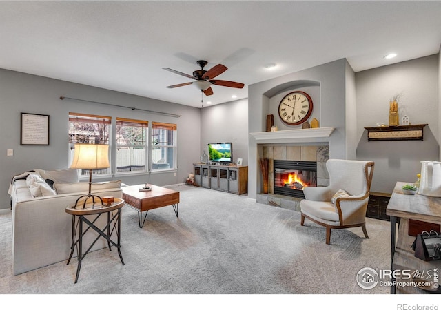 living room featuring ceiling fan, a tiled fireplace, and light carpet