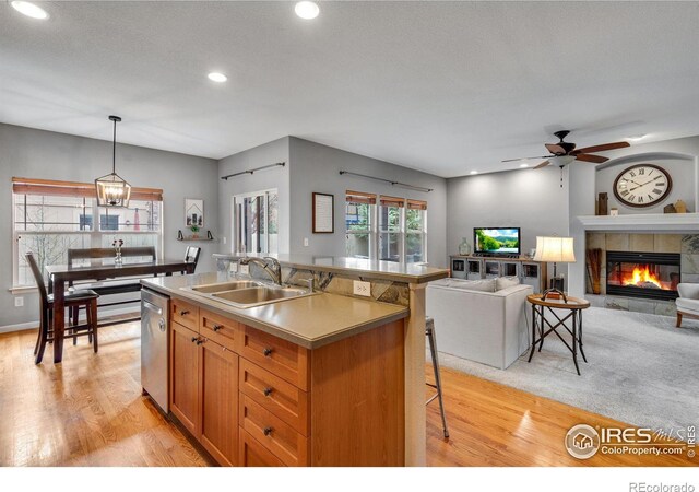 kitchen featuring ceiling fan with notable chandelier, a tiled fireplace, pendant lighting, a center island with sink, and sink