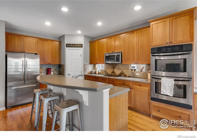 kitchen featuring light wood-type flooring, a center island, tasteful backsplash, a breakfast bar area, and stainless steel appliances