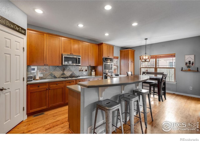 kitchen with pendant lighting, light hardwood / wood-style floors, appliances with stainless steel finishes, and a kitchen island