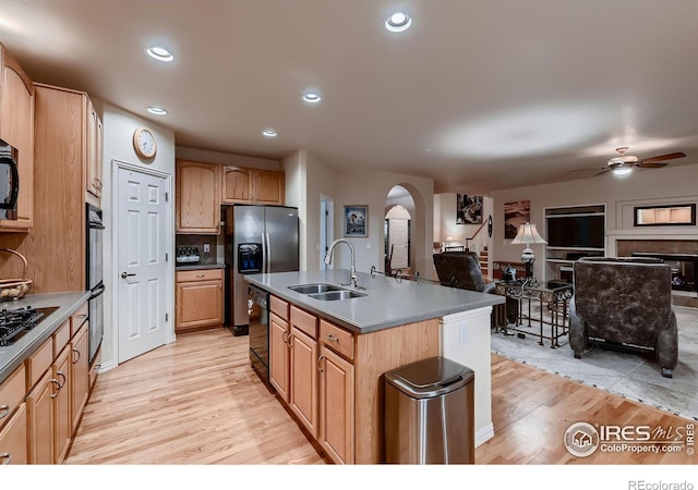 kitchen featuring ceiling fan, sink, black appliances, light hardwood / wood-style flooring, and an island with sink