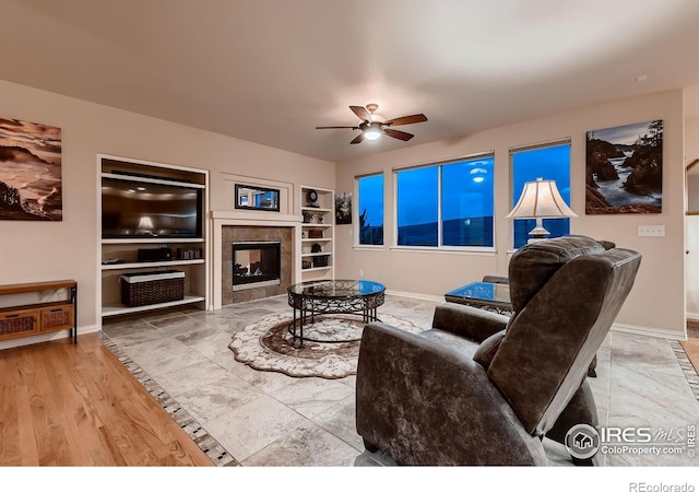 living room with built in shelves, ceiling fan, a tile fireplace, and hardwood / wood-style flooring