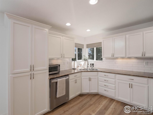 kitchen with dark stone counters, light wood-type flooring, sink, white cabinetry, and stainless steel dishwasher