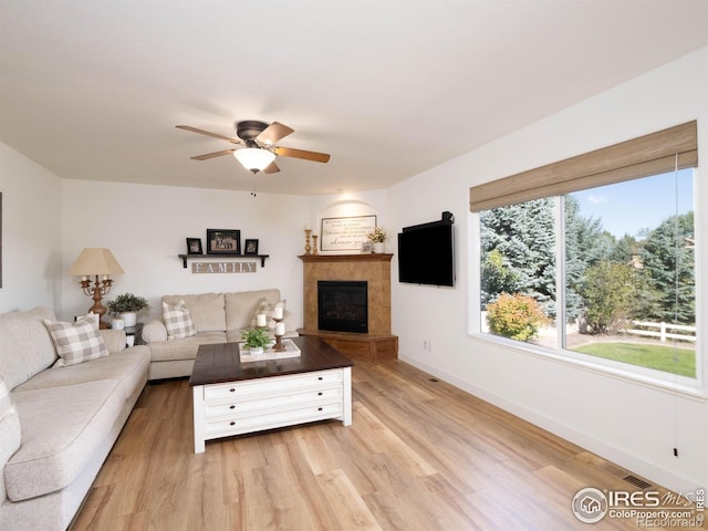 living room with a tile fireplace, ceiling fan, and light hardwood / wood-style flooring