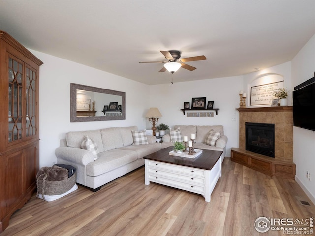 living room featuring a tile fireplace, light hardwood / wood-style floors, and ceiling fan