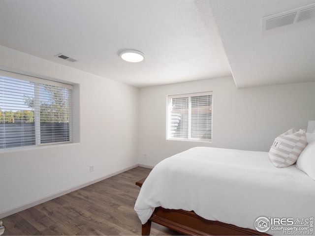 bedroom featuring multiple windows and dark hardwood / wood-style flooring