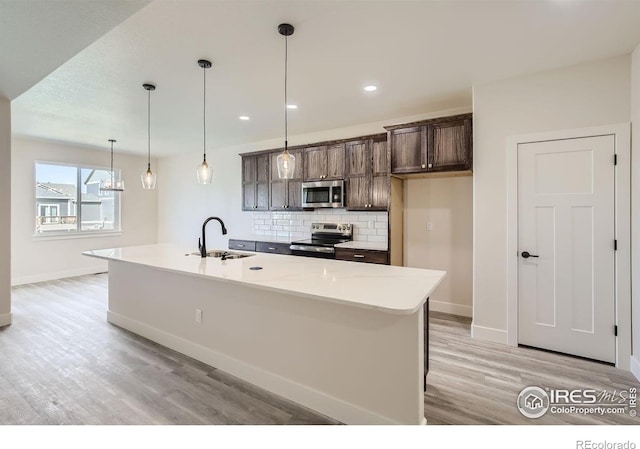 kitchen with light wood-type flooring, appliances with stainless steel finishes, a kitchen island with sink, and sink