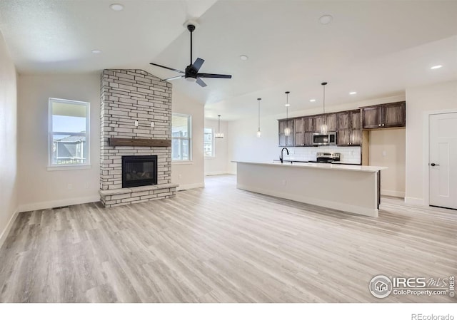 unfurnished living room featuring ceiling fan, light wood-type flooring, sink, a fireplace, and vaulted ceiling