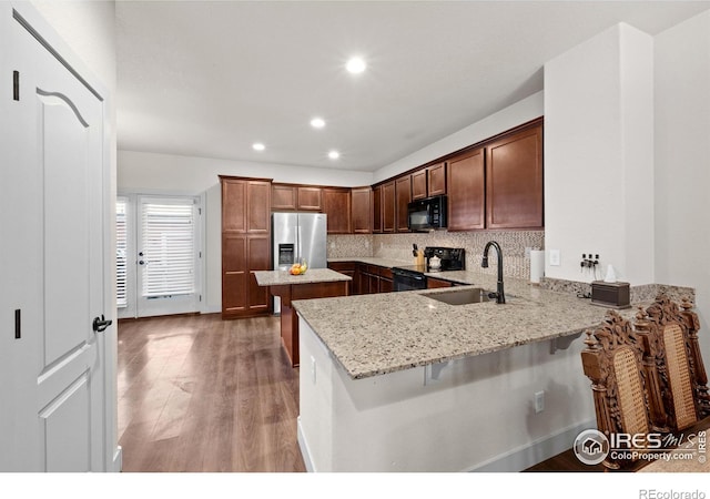 kitchen featuring light stone counters, sink, kitchen peninsula, a kitchen breakfast bar, and black appliances