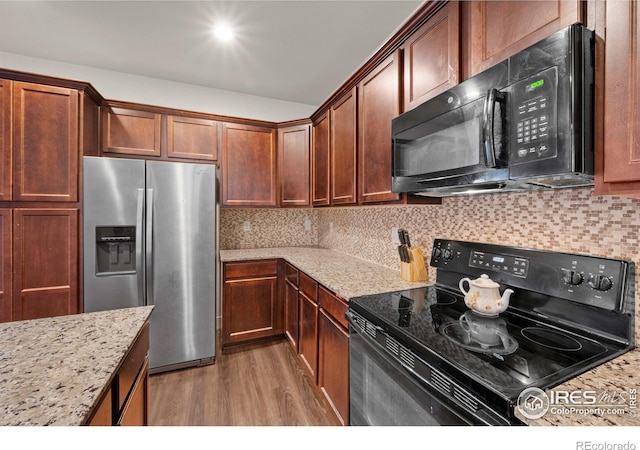 kitchen featuring light stone countertops, decorative backsplash, black appliances, and dark wood-type flooring