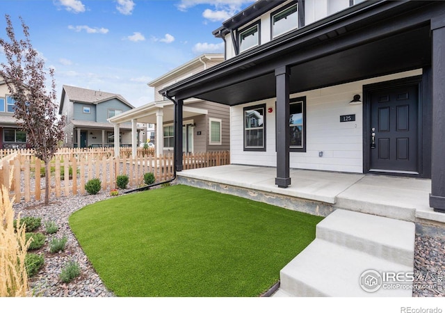 entrance to property featuring a yard, covered porch, and fence