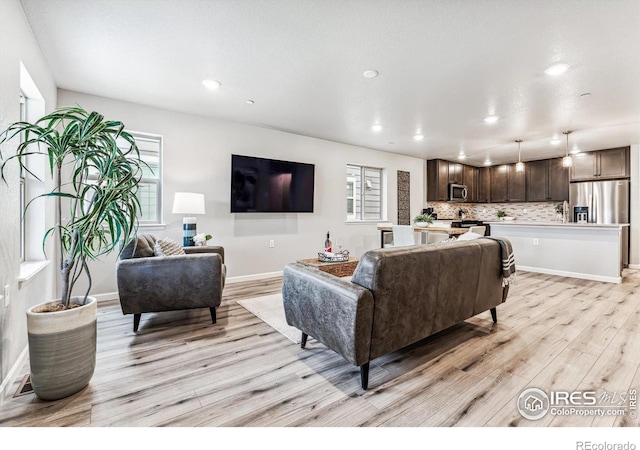 living area featuring plenty of natural light, baseboards, light wood finished floors, and recessed lighting
