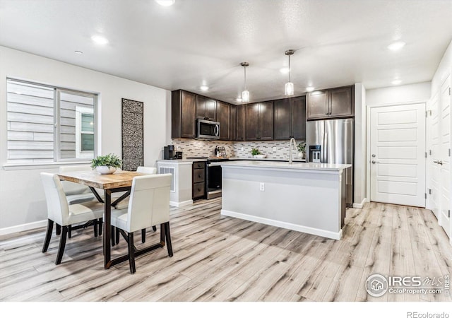 kitchen featuring light wood-type flooring, dark brown cabinetry, stainless steel appliances, and decorative light fixtures