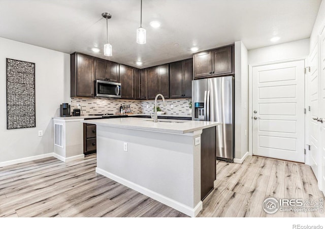 kitchen with appliances with stainless steel finishes, hanging light fixtures, dark brown cabinets, and light hardwood / wood-style flooring