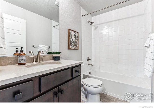 full bathroom with tile patterned flooring, a textured ceiling, vanity, tiled shower / bath, and toilet