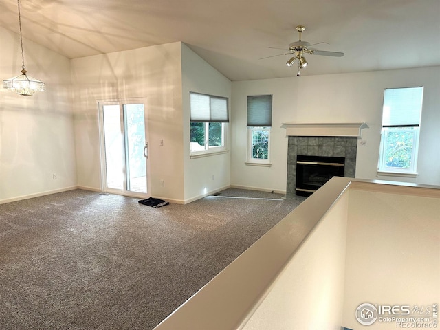 unfurnished living room featuring ceiling fan with notable chandelier, vaulted ceiling, a tile fireplace, and carpet floors