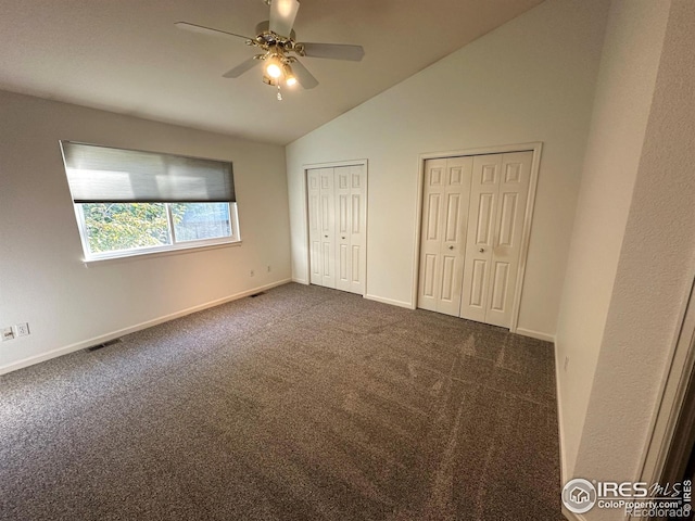 unfurnished bedroom with dark carpet, lofted ceiling, ceiling fan, and multiple closets