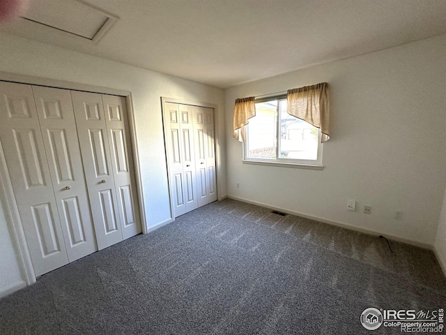 unfurnished bedroom featuring two closets and dark colored carpet