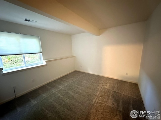 unfurnished room with beamed ceiling and dark colored carpet