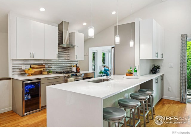 kitchen with beverage cooler, white cabinets, stainless steel range with gas cooktop, wall chimney range hood, and decorative light fixtures