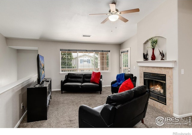 carpeted living room with a tiled fireplace and ceiling fan