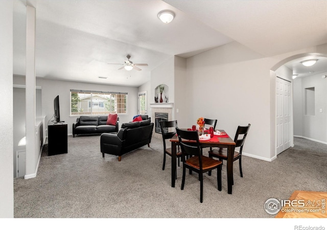 carpeted dining area featuring ceiling fan and a tiled fireplace