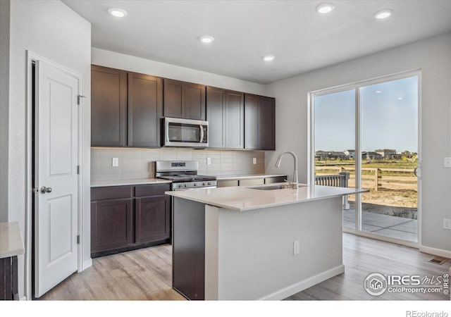 kitchen featuring appliances with stainless steel finishes, tasteful backsplash, light hardwood / wood-style flooring, dark brown cabinetry, and sink