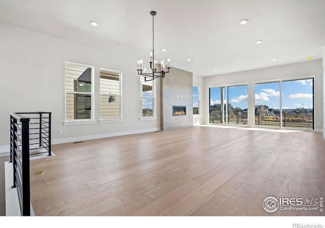 unfurnished living room featuring light hardwood / wood-style floors, a tiled fireplace, and a notable chandelier