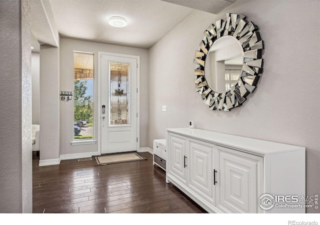 entryway with a textured wall, dark wood-type flooring, and baseboards