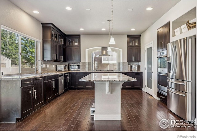 kitchen featuring stainless steel appliances, decorative backsplash, a kitchen island, wall chimney range hood, and a sink